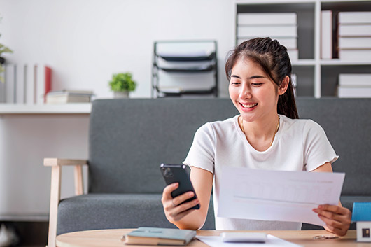 woman checking cellphone and document. Mobile and online banking